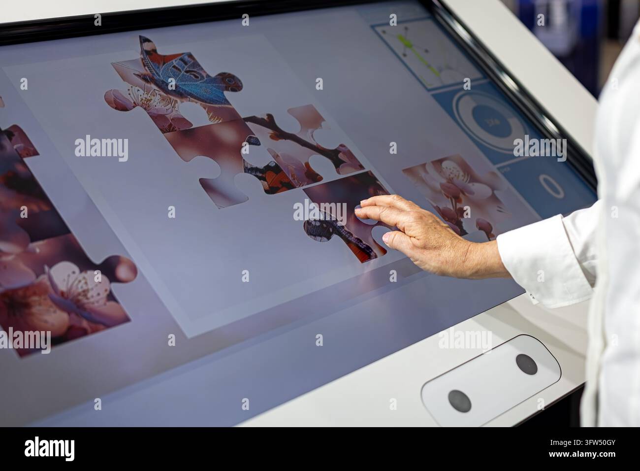 Seniorin löst ein digitales Puzzlespiel auf einem großen interaktiven Touchscreen-Display, kognitive Trainingsaktivität mit moderner Technologie für Stockfoto
