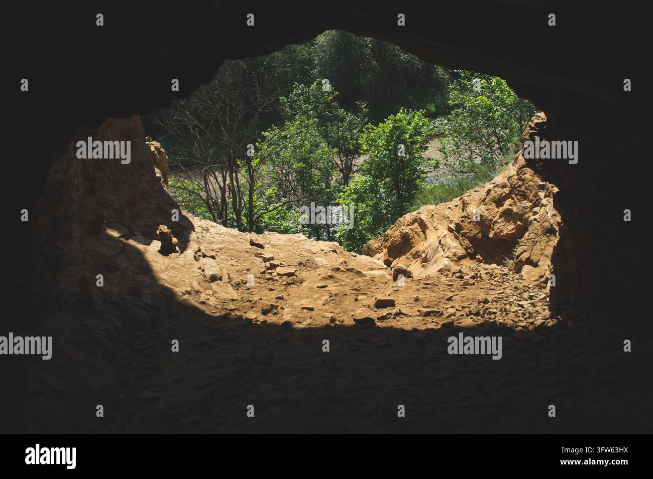 Eine Ansicht aus dem Inneren einer dunklen Höhle oder Grotte nach draußen. Die Ränder des Rahmens sind fast schwarz und bilden einen unregelmäßigen Bogen. Die Beleuchtung ist kontrastreich Stockfoto