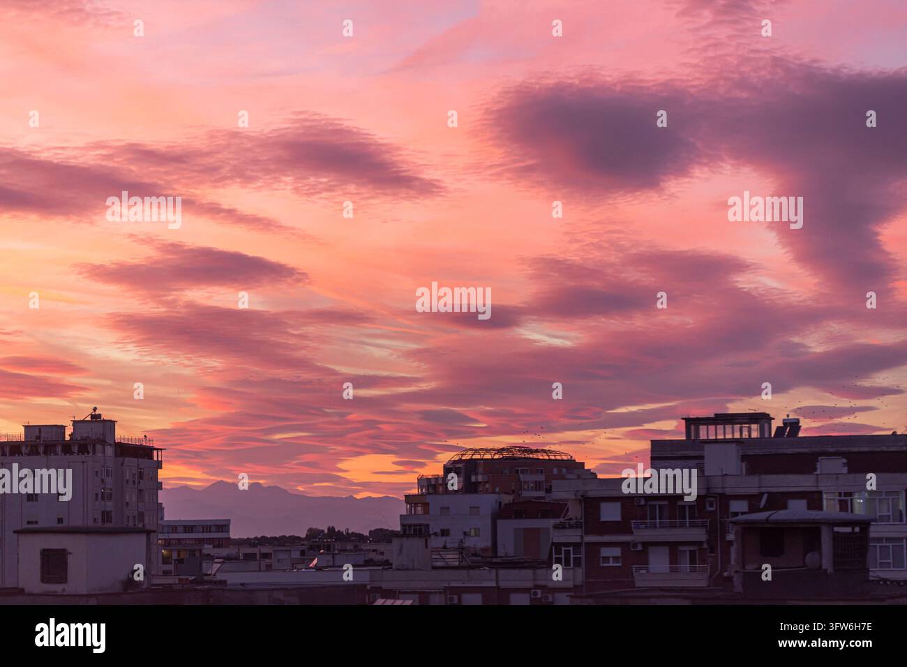 Albanien, Shkoder 2026 10 15: Weitwinkelaufnahme der städtischen Silhouettenlandschaft vor einem lebendigen Sonnenuntergangshimmel mit einzigartigen Wolken. Stockfoto