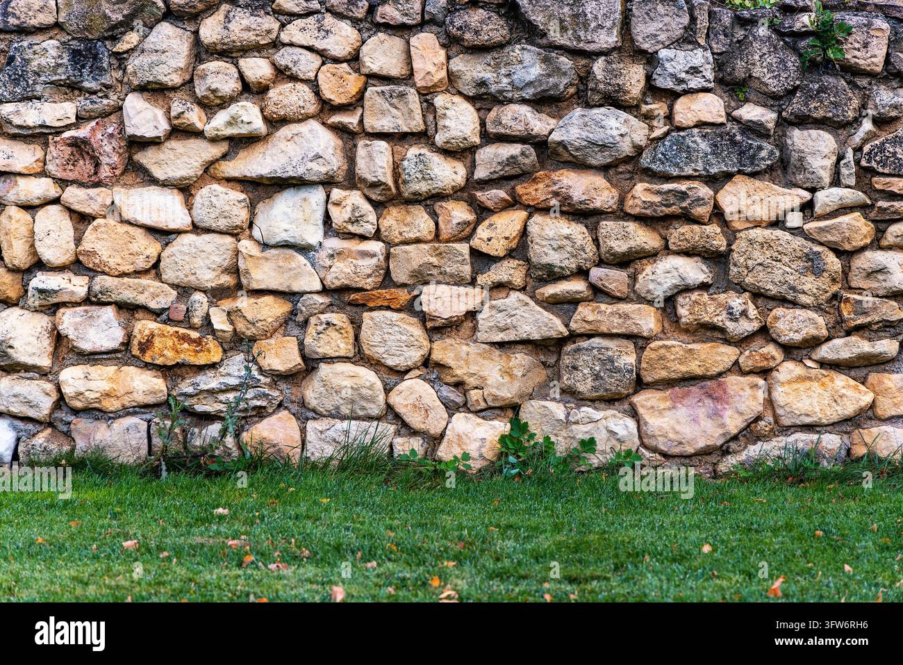 Alte rustikale Natursteinmauer-Hintergrundtextur mit grünem Rasengras am unteren Rand Stockfoto