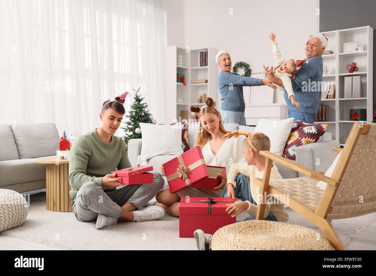 Weihnachtsfeier der Familie, mehrgenerationale Familie öffnet gemeinsam Geschenke in einem gemütlichen Wohnzimmer während der Winterferienzeit Stockfoto