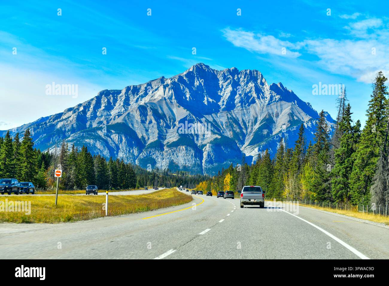 Panoramatische Ansicht von Autos, die auf dem Trans-Canada-Highway in Richtung des majestätischen Cascade Mountain unter einem strahlend blauen Himmel im Banff-Nationalpark, Alberta, fahren Stockfoto