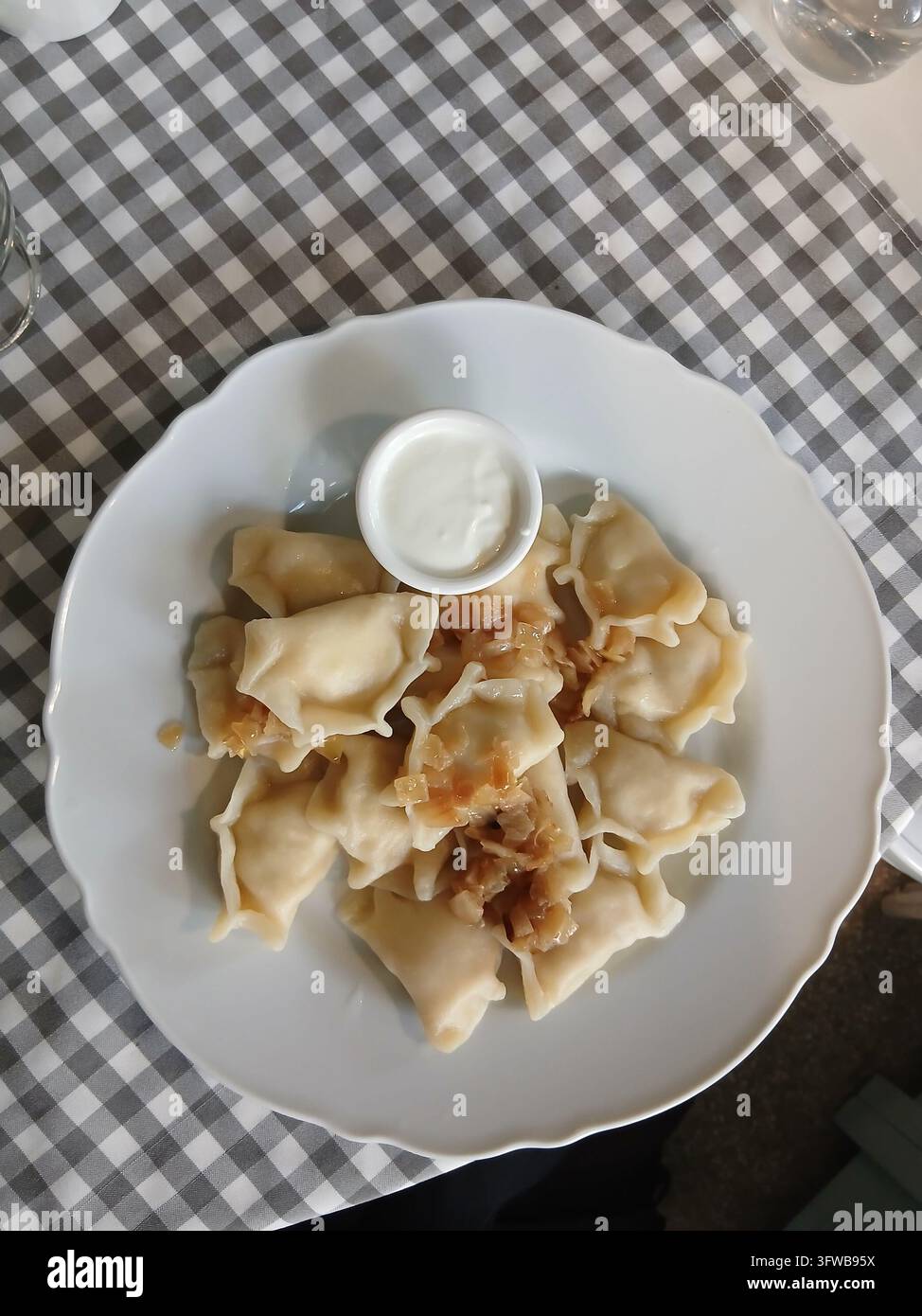 Eine detaillierte Ansicht von oben traditionelle osteuropäische Vareniki mit goldenen Zwiebeln und Sauce auf einer karierten Tischdecke. Stockfoto
