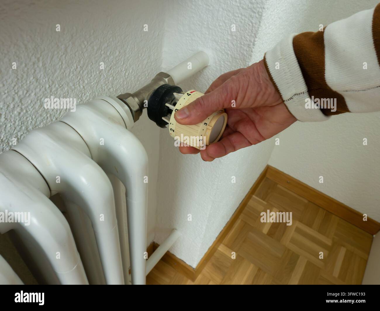 Seniorenhand, die den Heizkörperthermostat einstellt, um Energie zu sparen, Rentner senkt Heizkosten, steigende Nebenkostenrechnungen, Energiekrise und Haushaltsbudget c Stockfoto