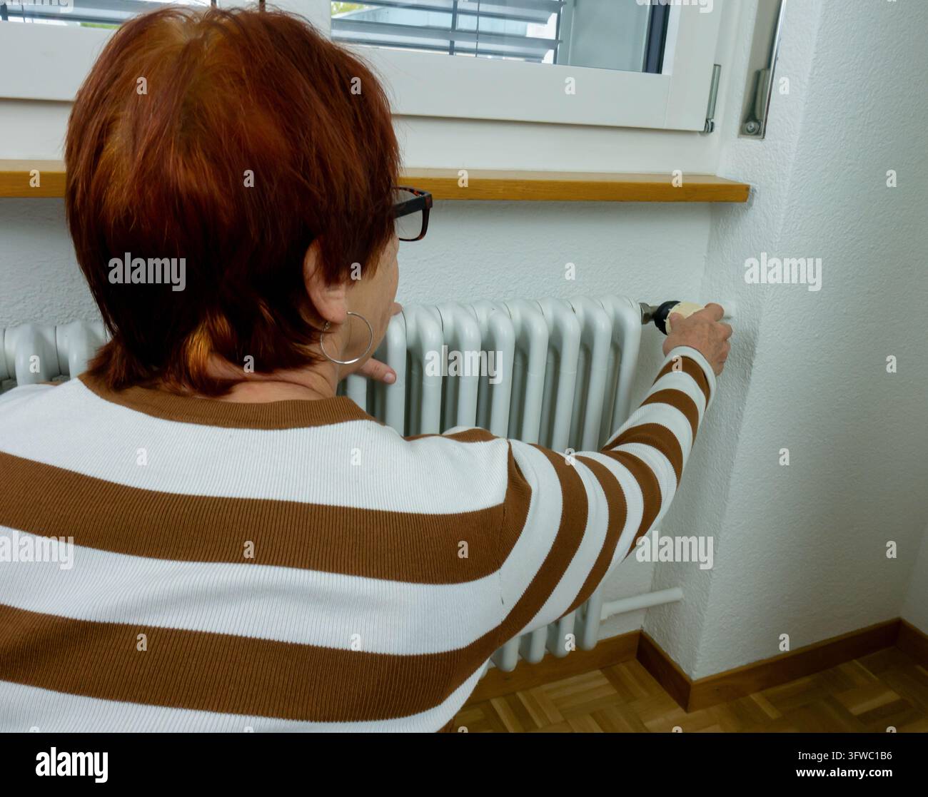 Seniorin dreht Heizungs-Thermostat, um die Heizung zu steuern, Rentnerin spart Energie und reduziert Winter-Heizkosten, Haushaltsbudget-Konzept Stockfoto