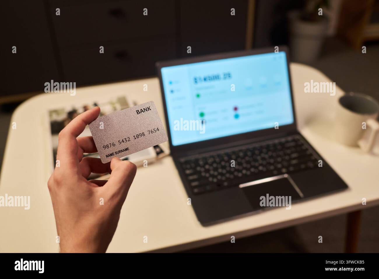 Hand eines Mannes, der eine Kreditkarte für Online-Banking auf einem Laptop hält Stockfoto