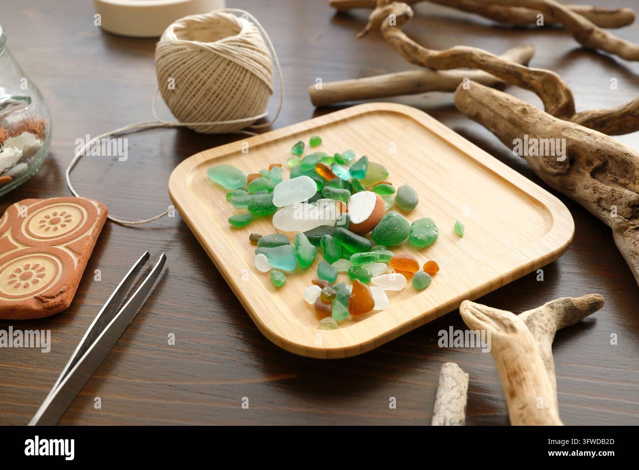Farbenfrohes Meerglas auf Holztablett mit Treibholz und Schnur. Flatlay Strandgut Bastelmaterialien mit Pinzette. Nachhaltig null Abfall Stockfoto