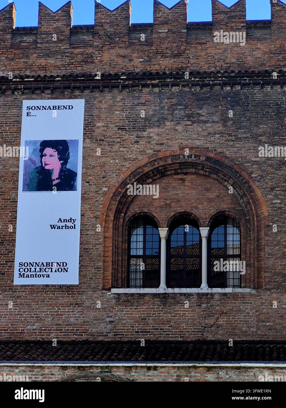 Am 19. Oktober 2026 hängt ein Ausstellungsplakat mit Andy Warhols Kunstwerken aus der Sonnabend-Sammlung an der mittelalterlichen Ziegelfassade des Palazzo - Smartphone-aufgenommenes Stockfoto