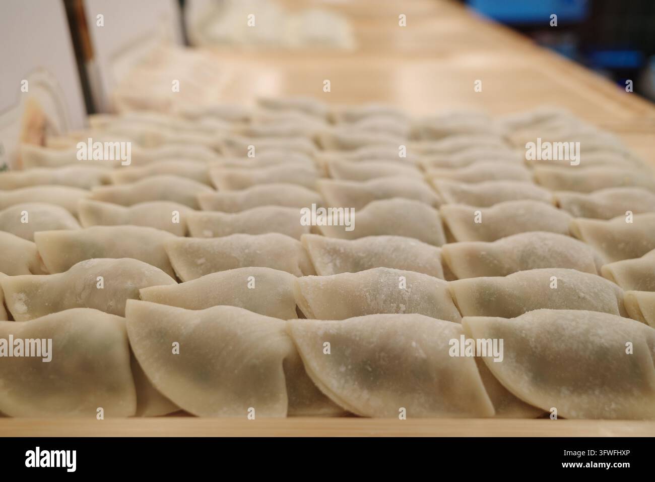 Nahaufnahme von rohen, gefalteten Knödeln, die in ordentlichen Reihen auf einer hölzernen Vorbereitungstafel in einer Restaurantküche angeordnet sind. Stockfoto