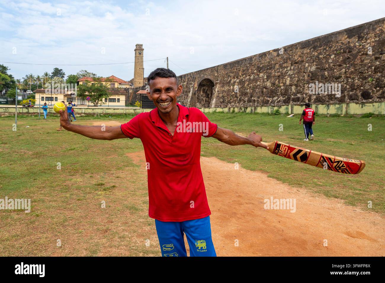 Lächelnder Mann hält einen Cricket-Schläger und einen Ball auf einem Feld unter den Festungsmauern, Südprovinz, Galle, Sri Lanka Stockfoto
