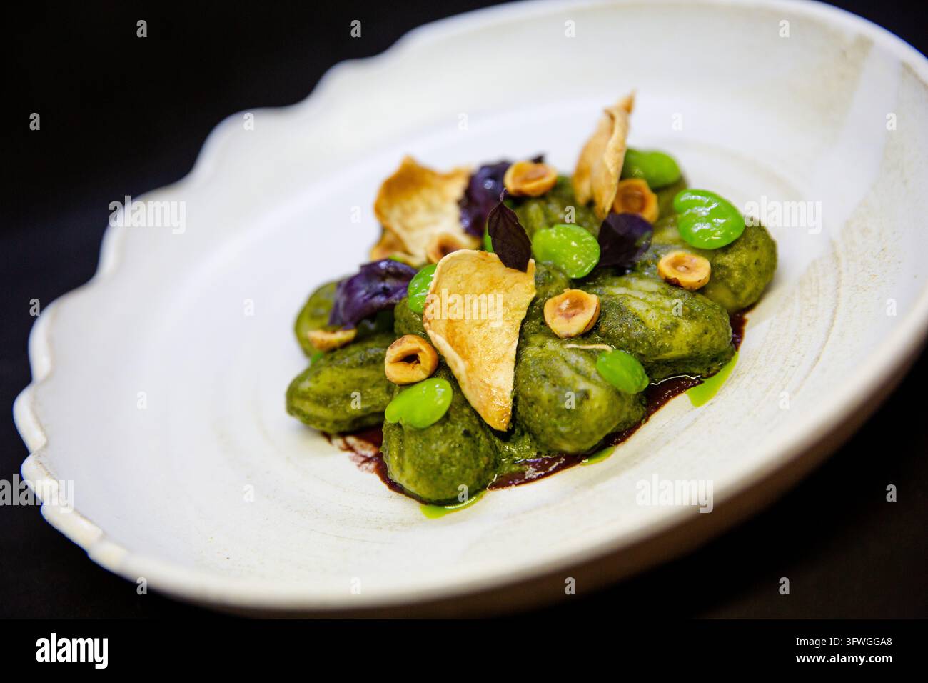 Grüne Gnocchi mit Edamame, gerösteten Haselnüssen, violettem Basilikum und knuspriger Garnitur in einer weißen Schüssel. Stockfoto