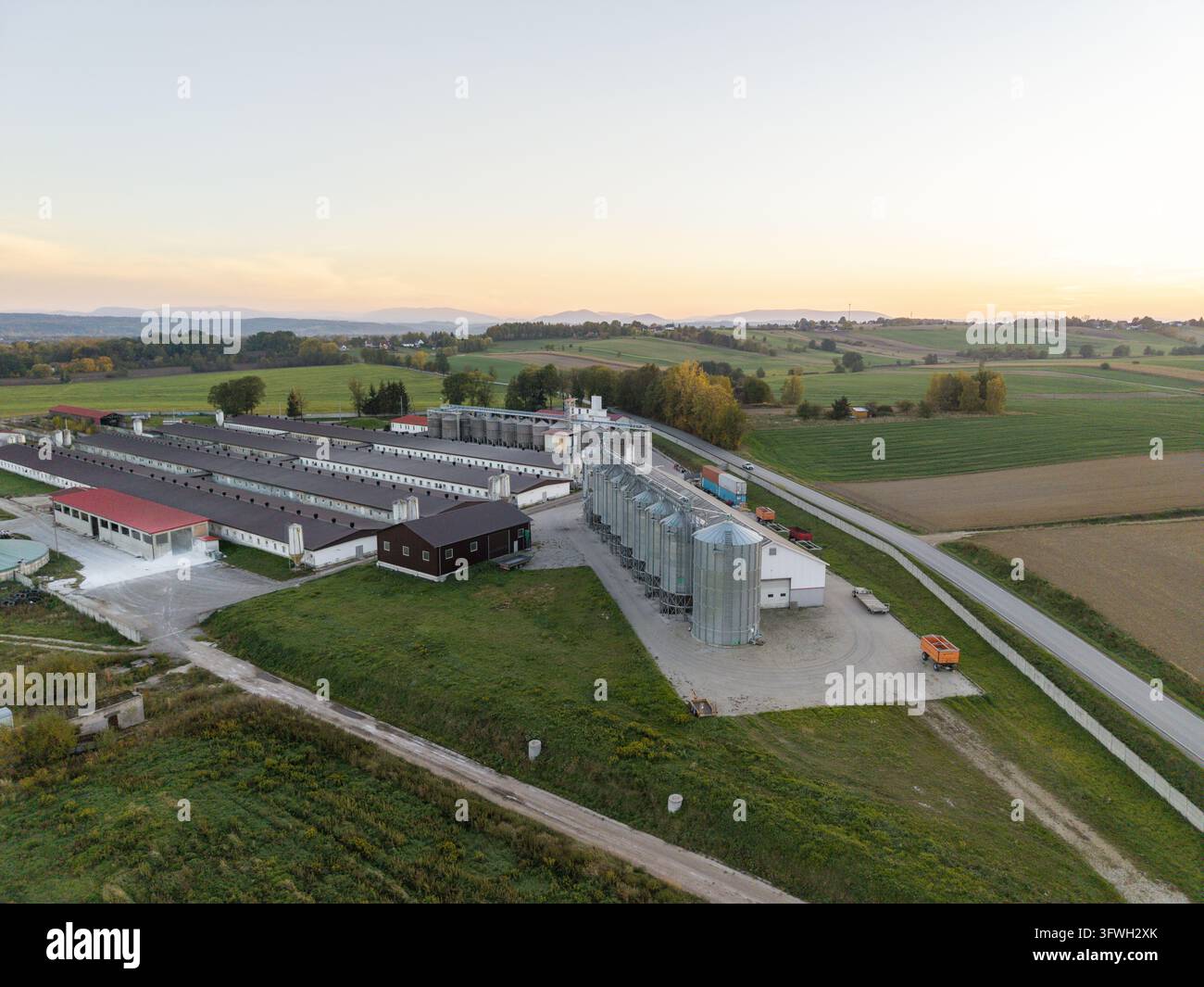 Luftaufnahme von Getreidesilos und langen landwirtschaftlichen Gebäuden, die sich unter den weiten Feldern der Landschaft der Woiwodschaft Kleinpolen in Polen befinden Stockfoto