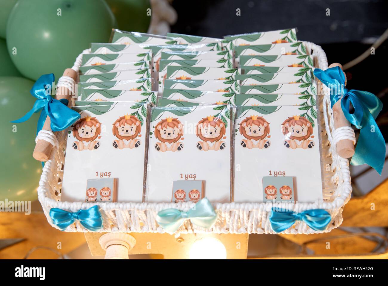 Niedliche Safari-Löwen-Themenpartygeschenke zum ersten Geburtstag eines Babys, wunderschön arrangiert in einem dekorativen Korb. Personalisierte Geschenkkarten und Souvenirs mit blau Stockfoto