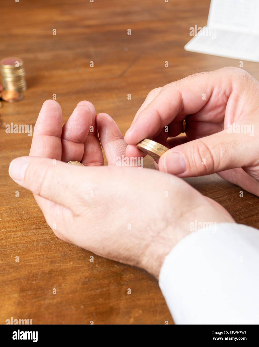 Nahaufnahme von Händen, die Münzen über einer offenen Handfläche auf einem Holztisch zählen, mit weiteren Münzen im Hintergrund, die persönliche Ersparnisse und Haushaltsbudget veranschaulichen Stockfoto