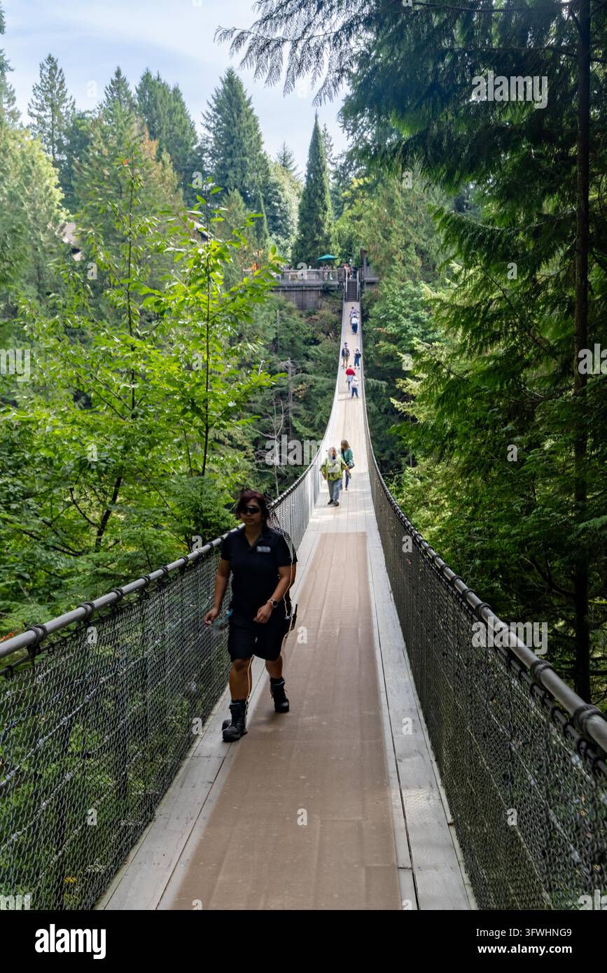 Vancouver, Kanada - 9. September 2026: Vertikale Perspektive von Besuchern, die die lange Hängefußgängerbrücke überqueren, die von Stahlmaschwerken und Zedernholz gesäumt ist Stockfoto