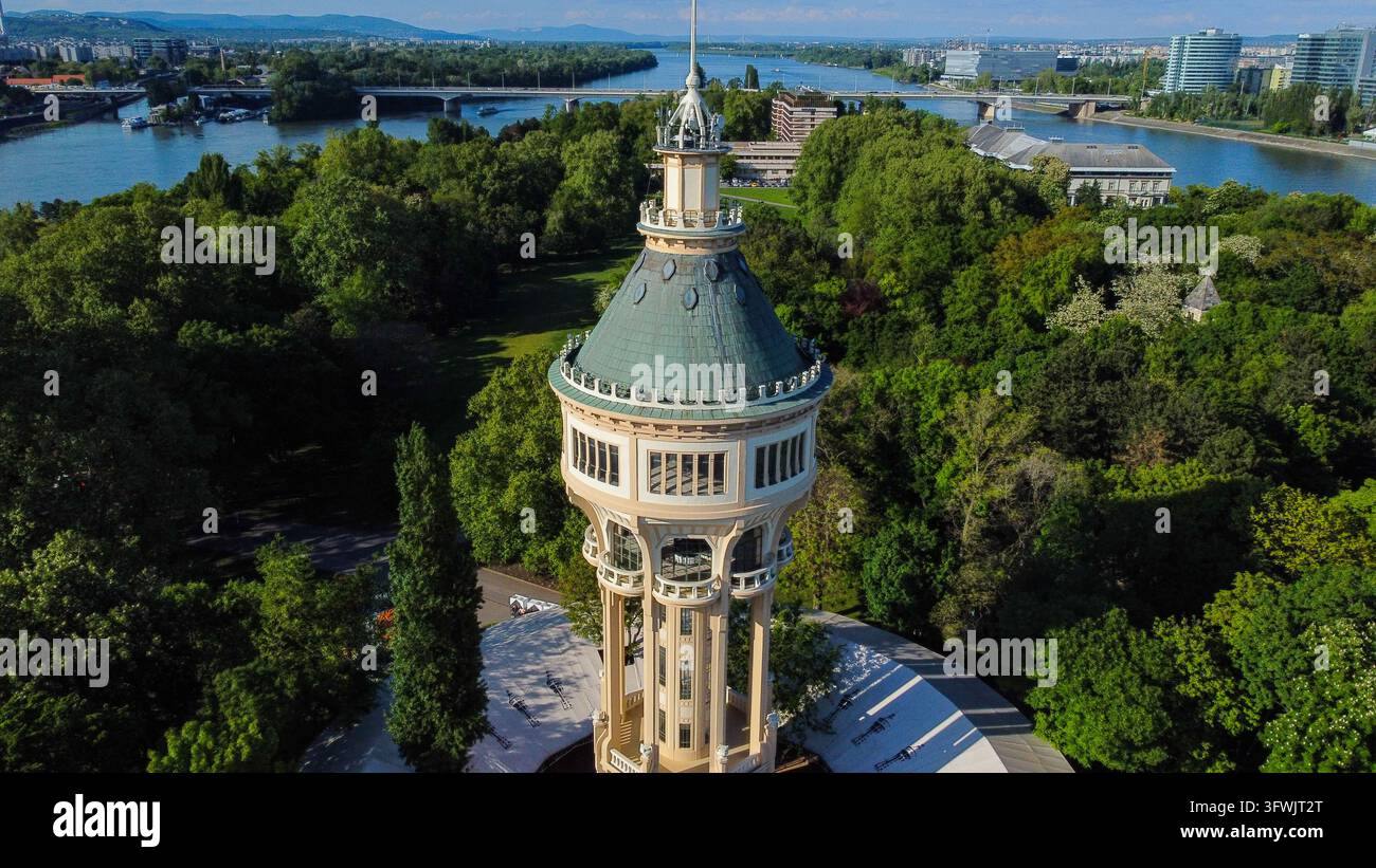 Luftbild des historischen Margaret-Insel-Wasserturms, umgeben von üppigen grünen Bäumen und Parkland, mit der Donau und der Stadt Skyline im Hintergrund Stockfoto