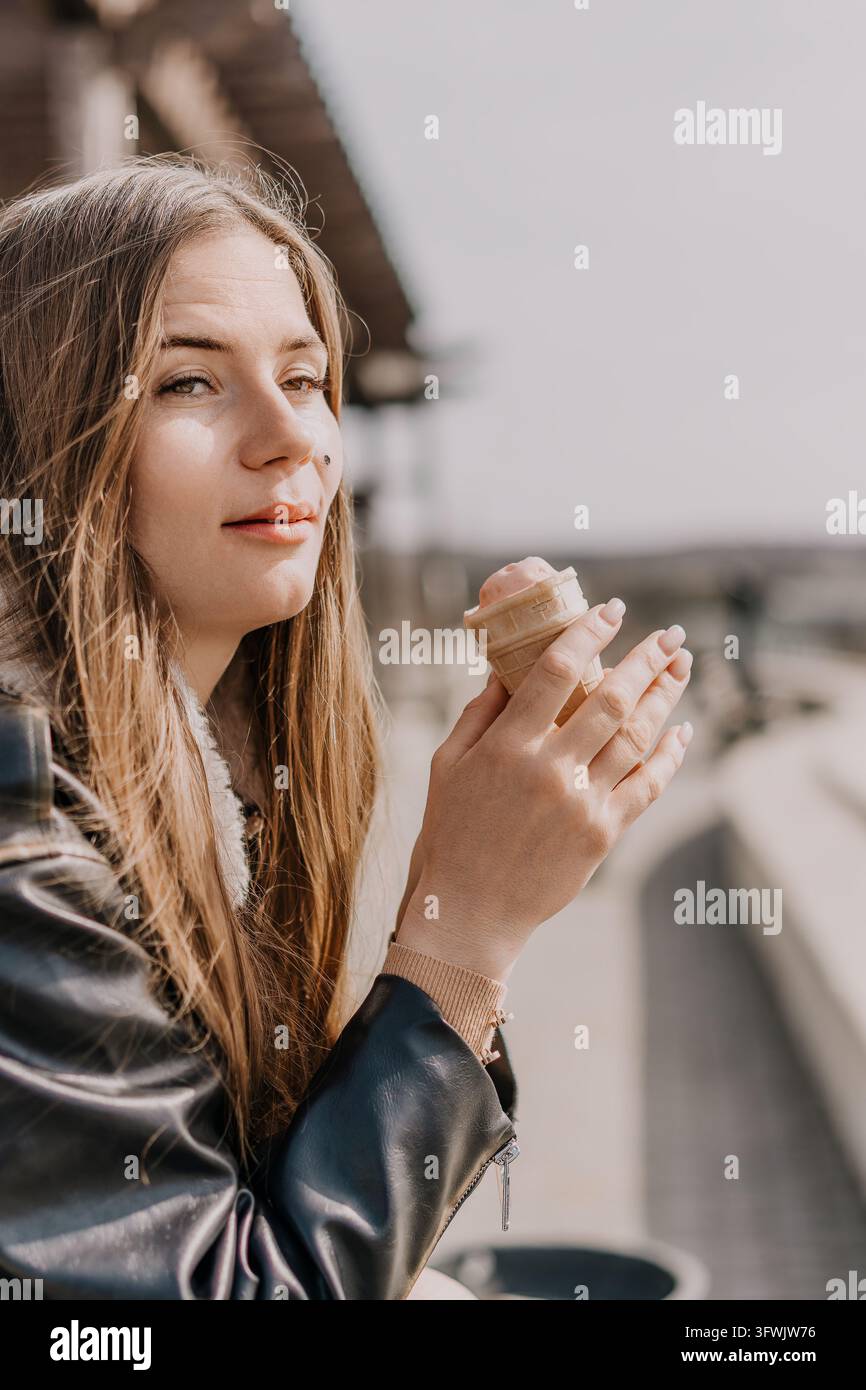 Junge blonde Frau mit einem Eisbecher, die draußen an einem hellen sonnigen Tag eine rosa Eisschöpfte in einer Waffeltasche hält Stockfoto