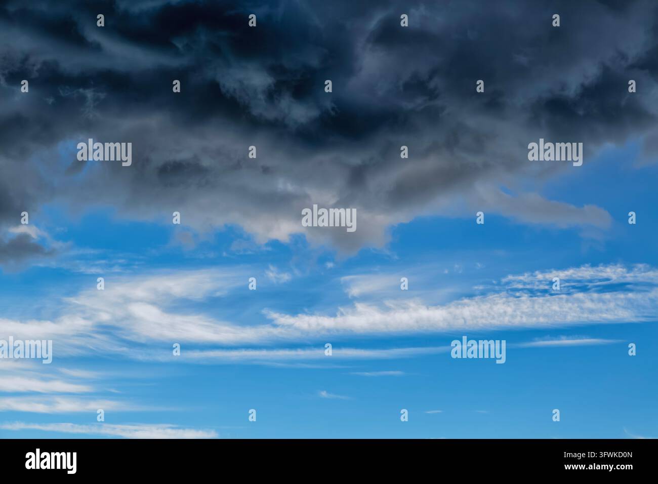 Dramatische Sturmwolken türmen sich über einem hellblauen Himmel mit zarten Zirrusstreifen darunter. Stockfoto