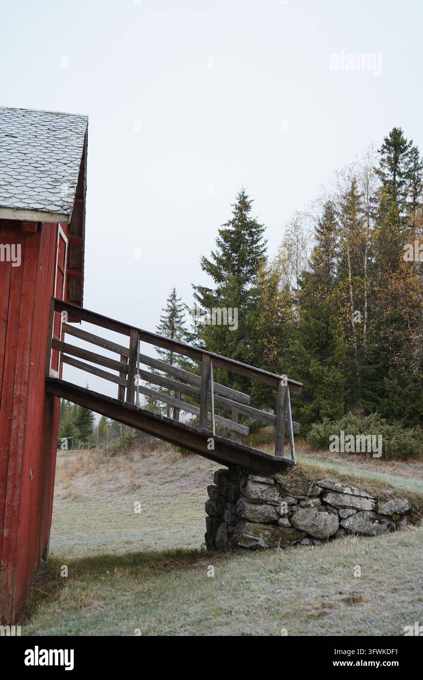 Traditioneller roter und rustikaler norwegischer Bauernhof mit Holzbrücke und Steinfundament in Valdres Stockfoto
