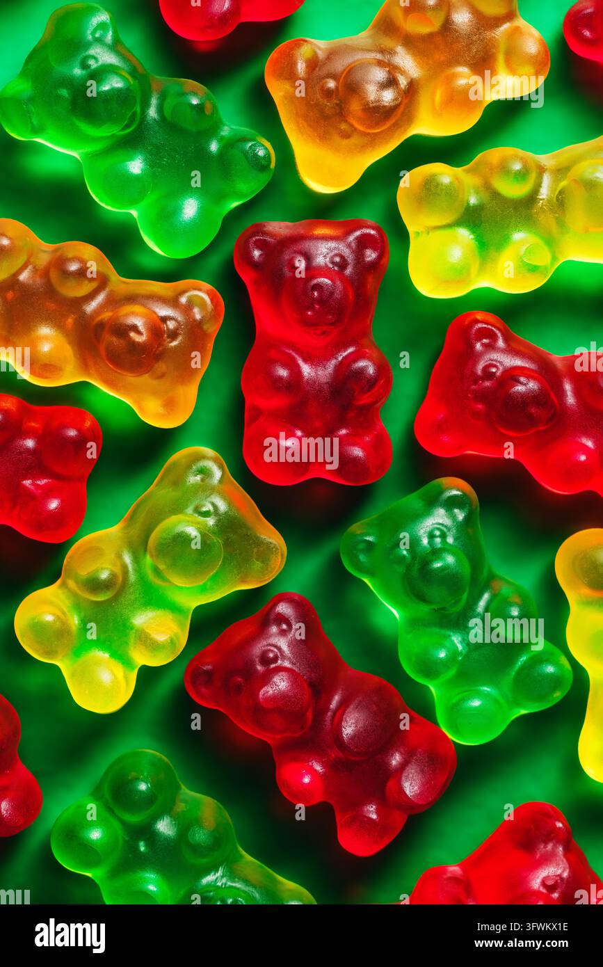 Roter Gummibärchen in der Mitte unter bunten Gummibonbons auf einem grünen Hintergrund Makro-Oberblick Stockfoto