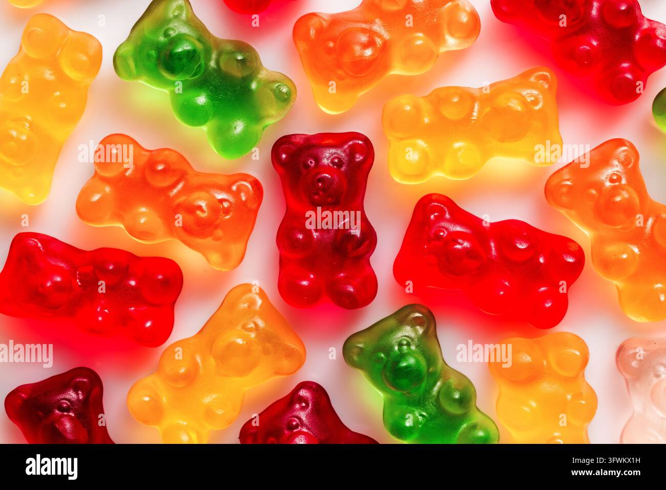 Roter Gummibärchen in der Mitte unter farbenfrohen Gummibonbons auf weißem Hintergrund, Makro-Ansicht von oben Stockfoto
