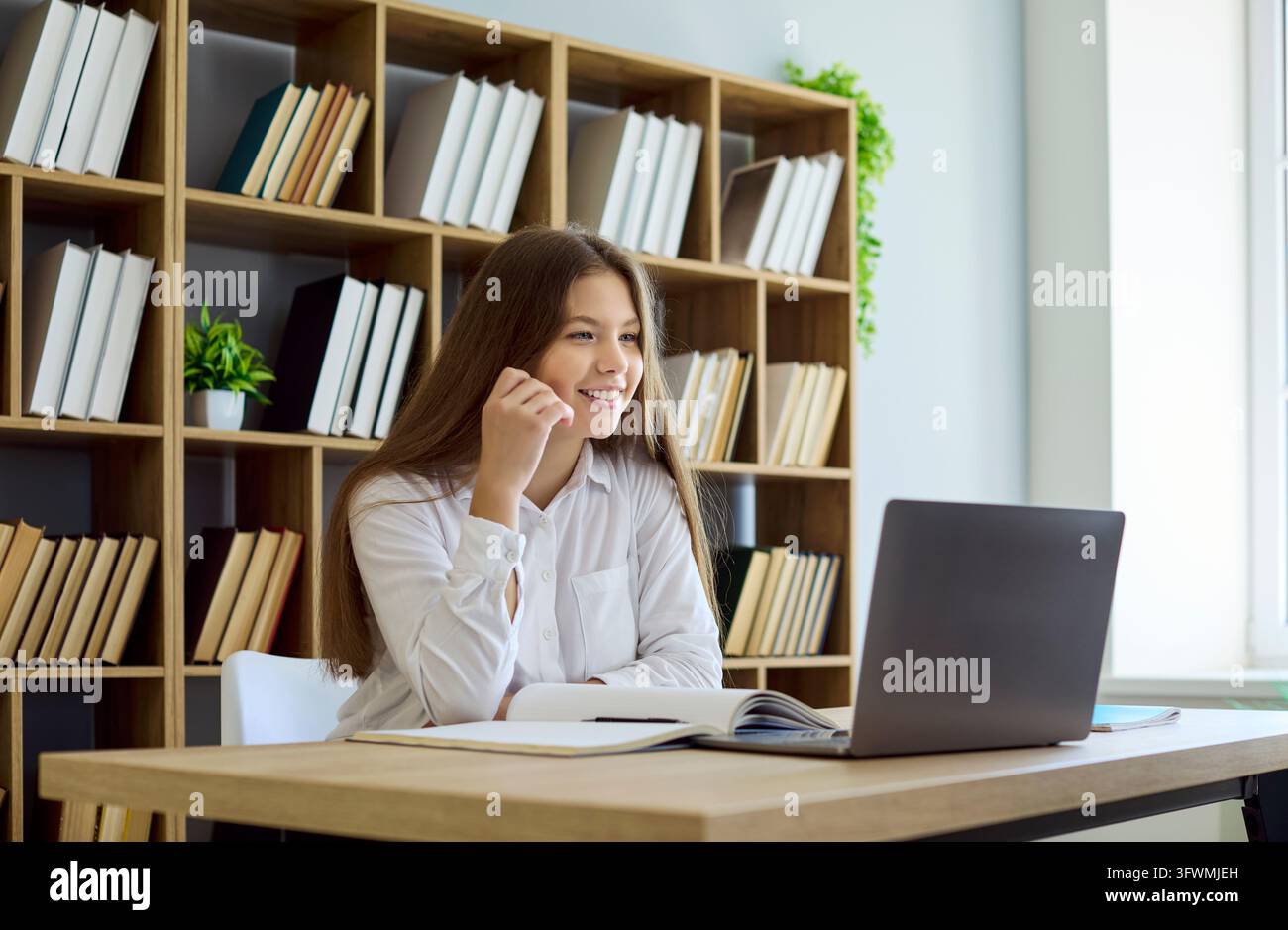 Lächelnder Student am Laptop in der Bibliothek während eines Online-Kurses und einer Videoanruf-Sitzung Stockfoto