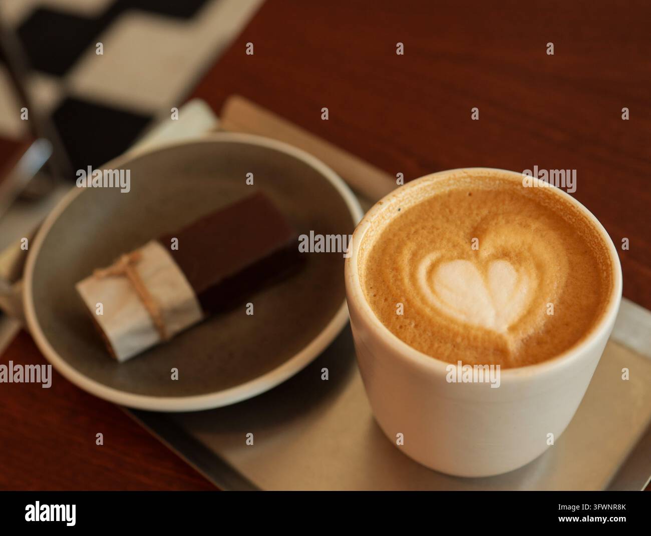 Hochwinkel-Makroaufnahme von herzförmiger Latte-Art auf einer Tasse Cappuccino-Kaffee in der Nähe eines Desserts. Stockfoto