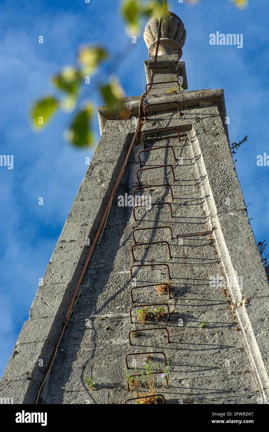 Kirchturmspitze mit einer traditionellen Metallleiter, die vertikal an ihrer konischen Seite montiert ist, vor einem blauen Himmel. Stockfoto
