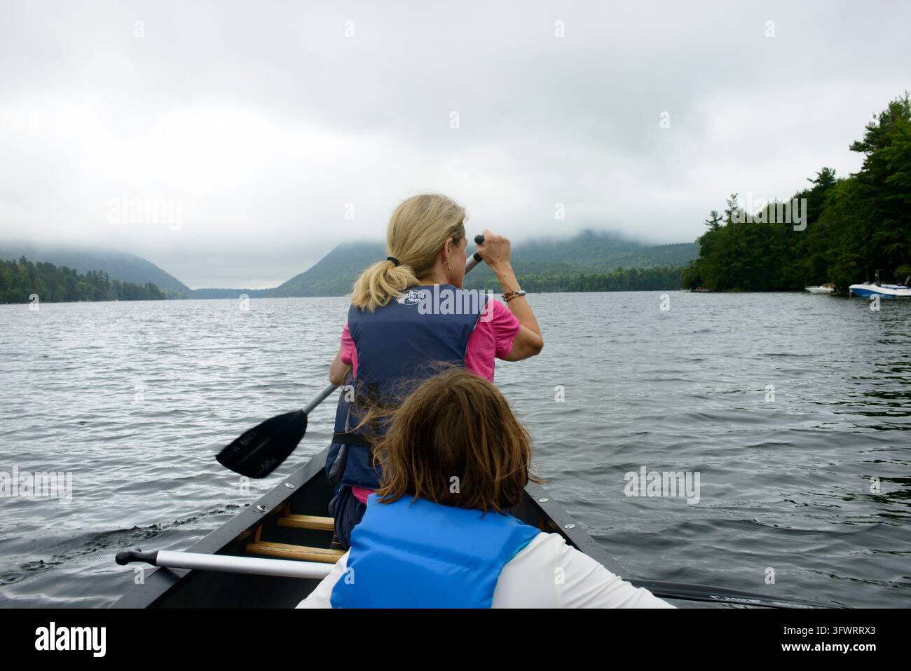 Rückansicht von Mutter und Kind, die auf einem See an einem bewölkten Tag Kanu paddeln Stockfoto