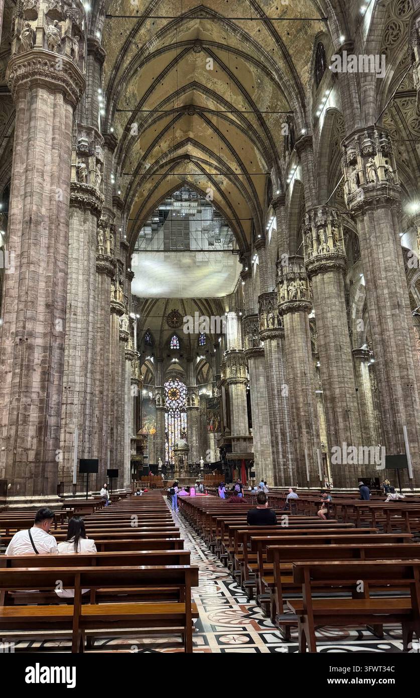 Mailand, Italien, 21. Juli 2024: Reihen von Holzbanken führen zum Altar unter gewölbten Steingewölben, geschmückte Säulen in der Kathedrale Duomo di Milano Stockfoto