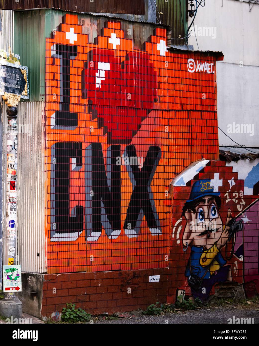 Chiang Mai, Thailand - 17. Januar 2026: Ein lebhaftes Straßenkunst-Mural mit pixelierten Grafiken und einer Cartoonfigur, die auf Wellblech gemalt ist… Stockfoto