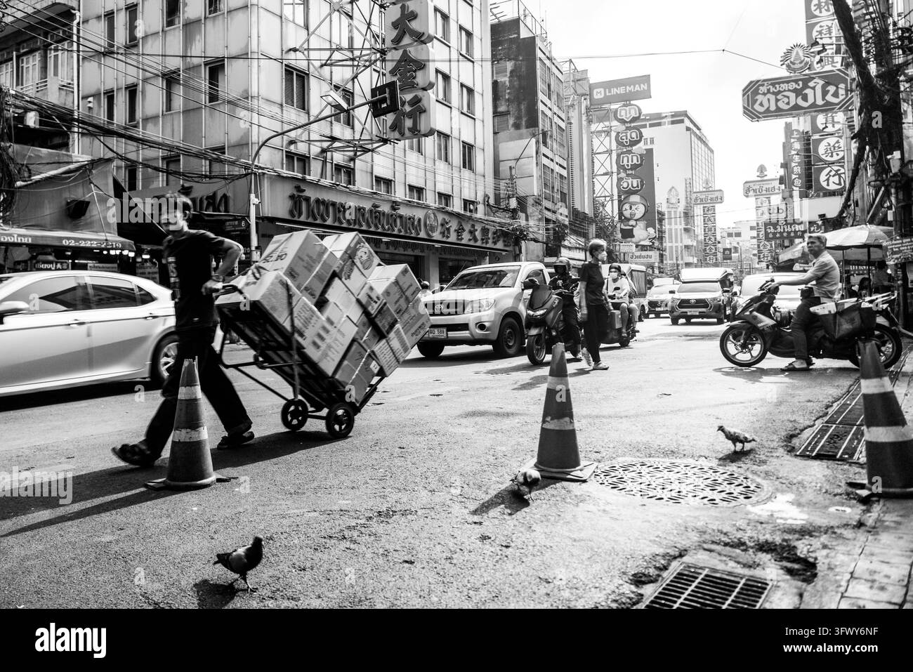 Bangkok, Thailand - 31. Januar 2026: Schwarz-Weiß-Foto einer belebten Stadtstraße mit Menschen zu Fuß, Fahrzeugen, Motorrädern, Tauben und einem... Stockfoto