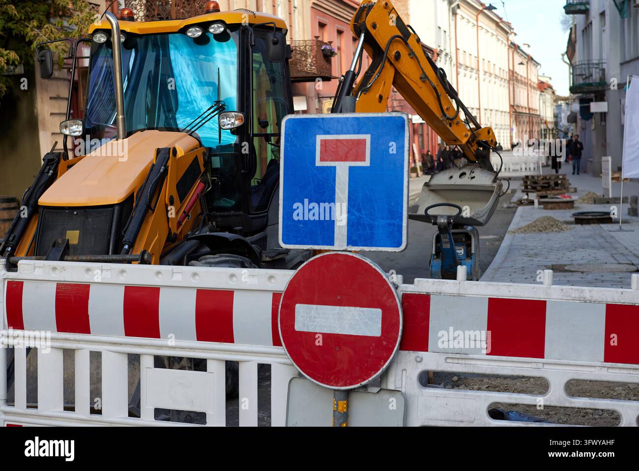 Straßenbau mit Bagger, Verkehrsschildern und Einfahrtsverbotsschild auf einer städtischen Straße. Straßenarbeiten stellen Infrastrukturreparatur und Straßenwartung dar Stockfoto