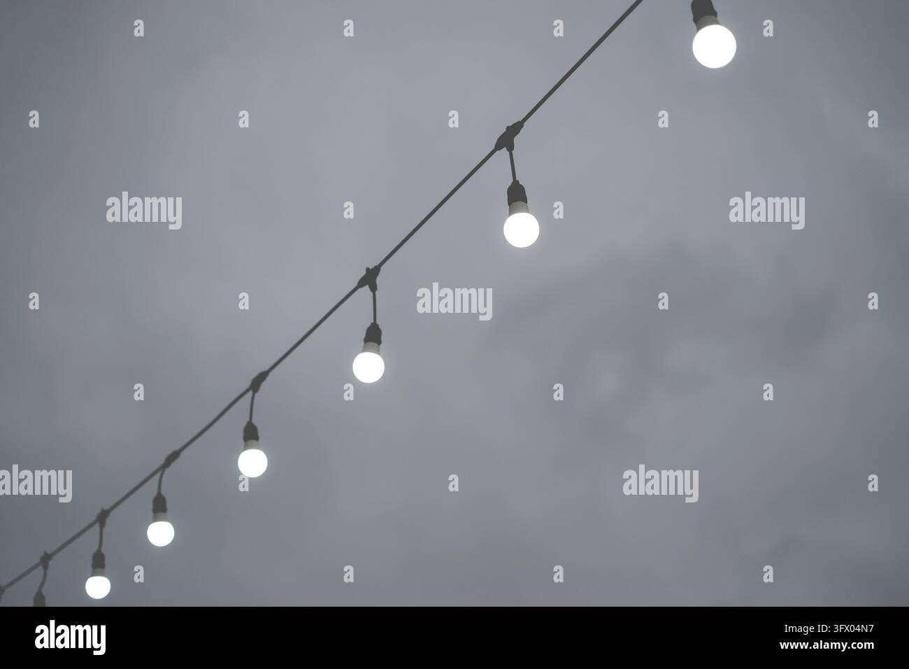 Leuchtende Außenlichterketten, die sich vor einem bewölkten Abendhimmel abheben Stockfoto