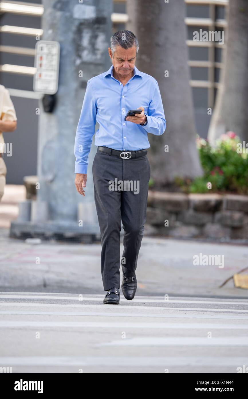 Brickell, FL, USA - 20. Oktober 2026: Geschäftsmann in einem blauen Hemd überquert die Brickell Avenue in Miami Stockfoto