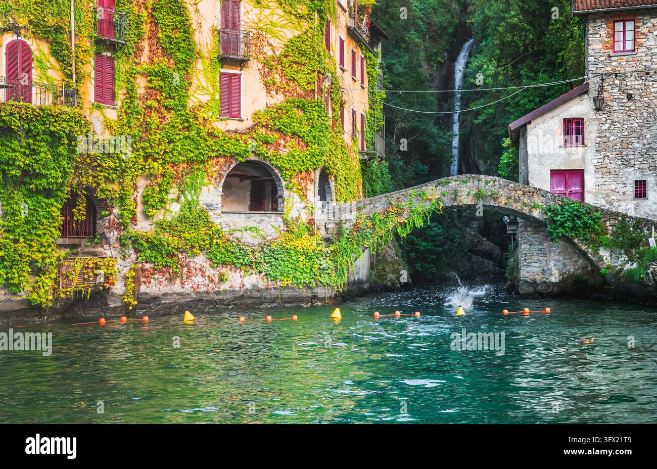 Steinerne Bogenbrücke im Dorf Nesso mit von Efeu überwucherten Gebäuden und Wasserfall am Comer See, Lombardei, Italien Stockfoto