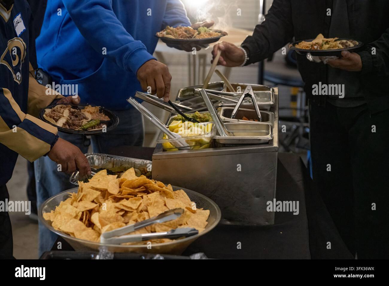 Die Buffetlinie ist voller hungriger Kunden, die mit den Servierzangen ihre Teller füllen. Stockfoto