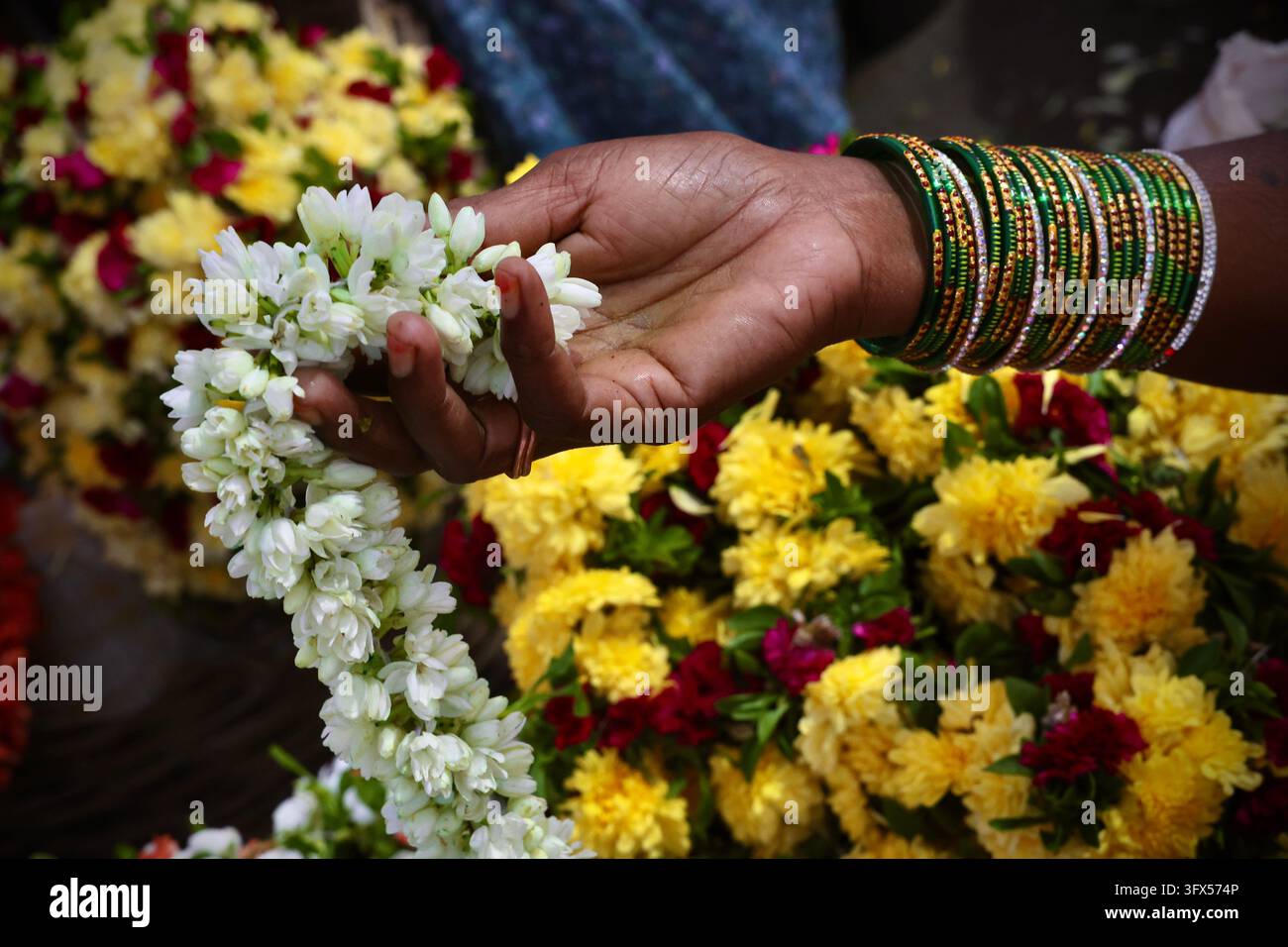 Hand mit grünen und goldenen Armreifen, die einen weißen Jasmin-Girlande über Ringelblumen hält Stockfoto