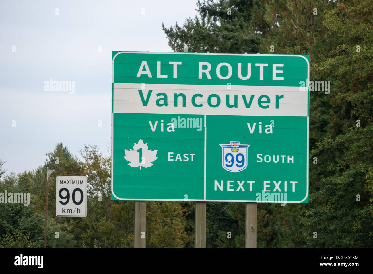 Vancouver, Kanada – 9. September 2026: Horizontale Augenhöhe-Aufnahme eines grünen Richtungsschilds für Autobahnen und eines Geschwindigkeitsbegrenzungsschilds neben Nadelhölzern. Stockfoto