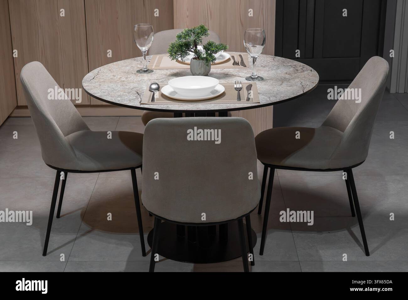 Moderner Essbereich mit einem runden Marmortisch, gepolsterten beigen Stühlen und minimalistischer Holzschrankfront in einem zeitgenössischen Interieur Stockfoto