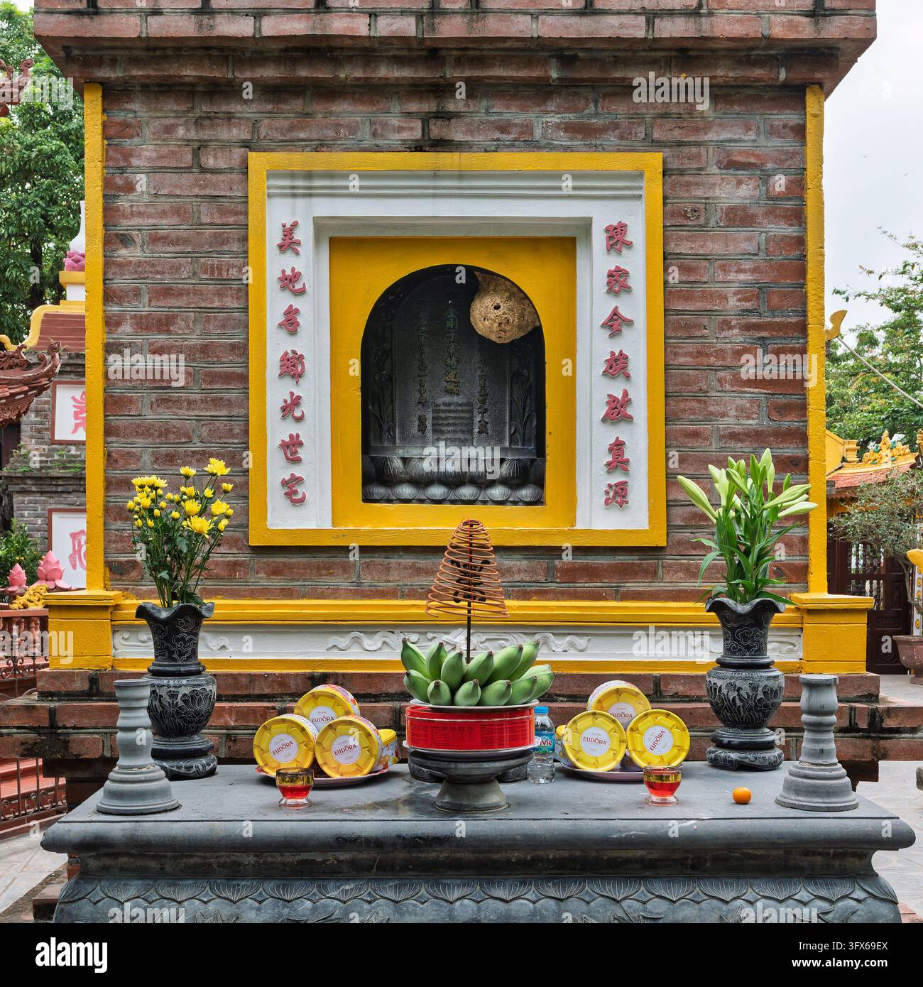 Hanoi, Vietnam - 20. April 2026: Gaben mit Weihrauch, Blumen und Obst auf einem Altar vor einem Ziegel-Schrein in der Tran-Quoc-Pagode Stockfoto