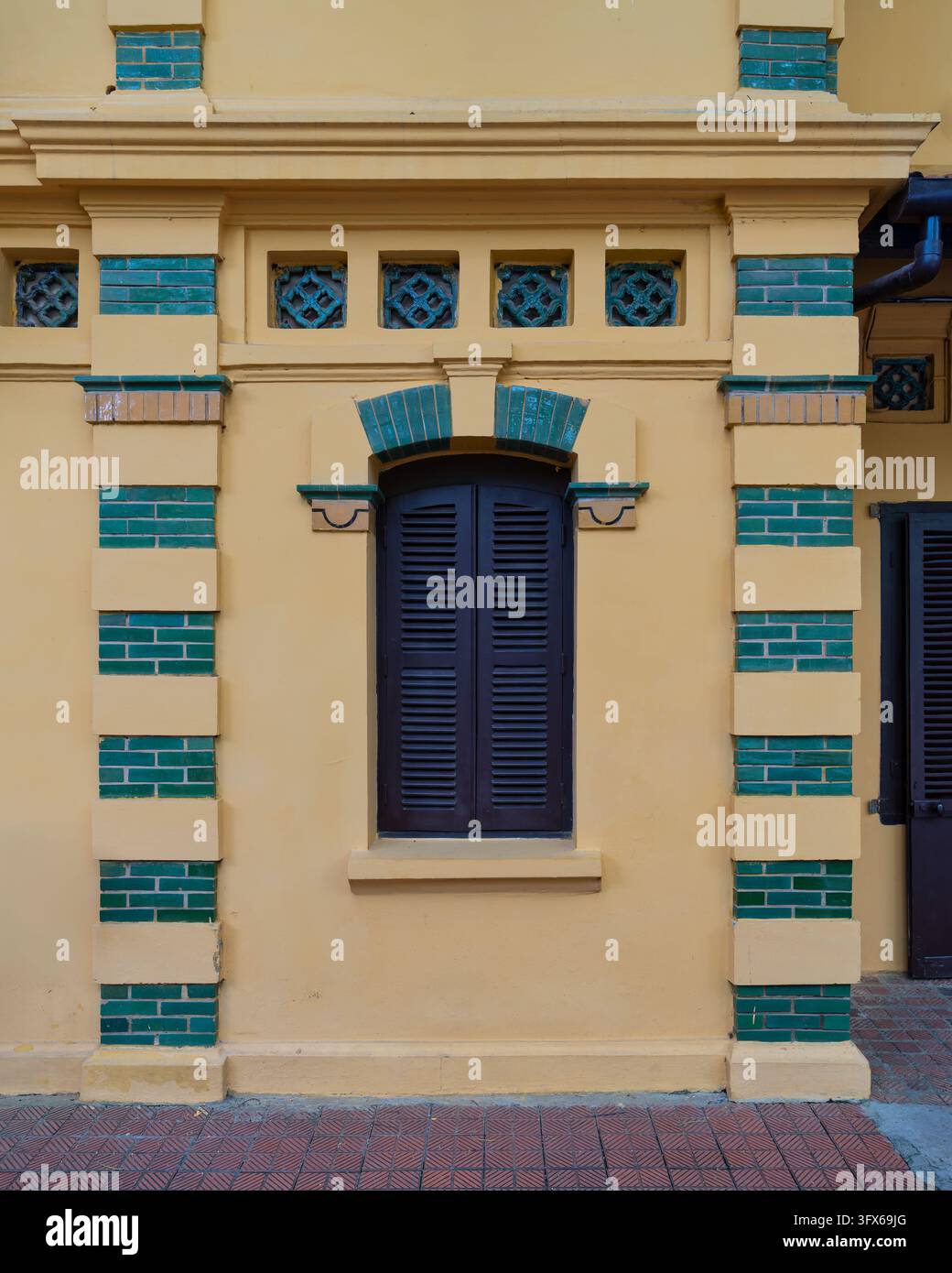 Französisches koloniales Architekturdetail mit gelben Wänden, grünen Backsteinakzenten und einem dunkelbraunen Fenster mit Läden im Präsidentenpalast in Hano Stockfoto