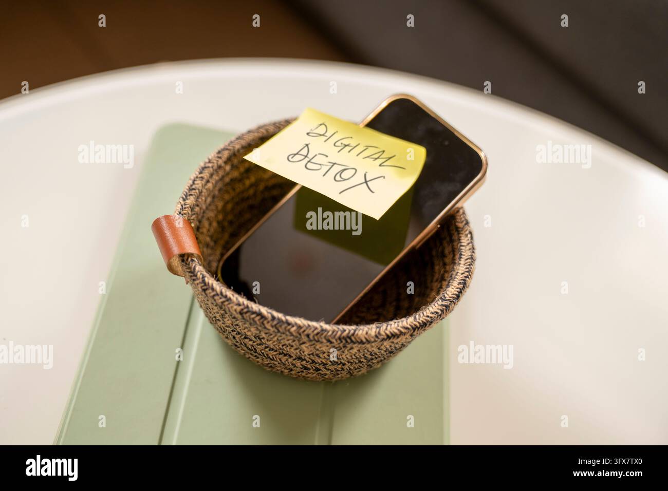 Nahaufnahme eines Smartphones, das in einem geflochtenen Korb über einem Tablet platziert ist, mit einer handgeschriebenen Digital-Detox-Notiz. Konzept des Technologiepauses, rot Stockfoto