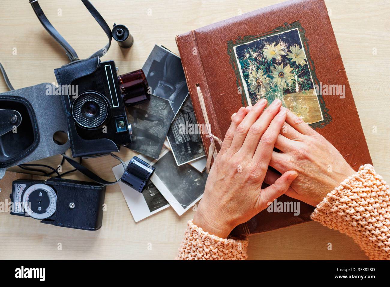 Hände, die auf einem Vintage-Fotoalbum ruhen, umgeben von alten Schwarz-Weiß-Fotografien, Filmkamera, Fotofilm, Lichtmesser. Nostalgie, Erinnerungen, Stockfoto