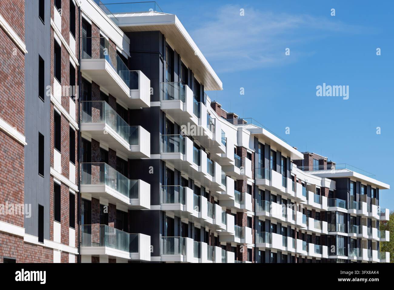 Modernes Wohngebäude mit Glasbalkonen und Ziegelfassade steht unter klarem blauem Himmel und symbolisiert urbanen Komfort und zeitgenössisches Wohnen. Stockfoto