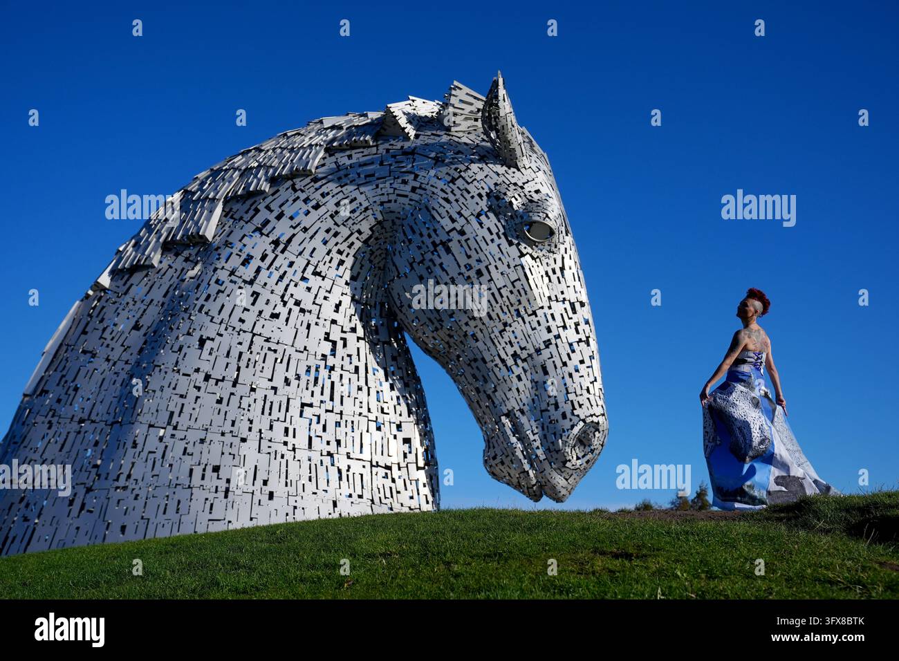 Model Daniela Margiotta, neben den Kelpies in Falkirk, trägt ein Kleid der Modedesignerin Alison Harm aus fotografischem Leinwandmaterial, das ein Bild der Kelpies von Sharon McMenemy Khan zeigt, das auf der diesjährigen ReFashion Edinburgh vorgestellt wird, einer nachhaltigen Modeveranstaltung in der Biscuit Factory in Edinburgh am Sonntag, den 15. November 2026. ReFashion Edinburgh ist eine Graswurzel-Bewegung für nachhaltige Mode, die dazu gedacht ist, die Umwelt Schäden des Fast-Fashions zu bekämpfen und eine kreative Plattform für langsame, ethische Kleidungsherstellung zu bieten. Bilddatum: Donnerstag, 22. Oktober 2026. Stockfoto