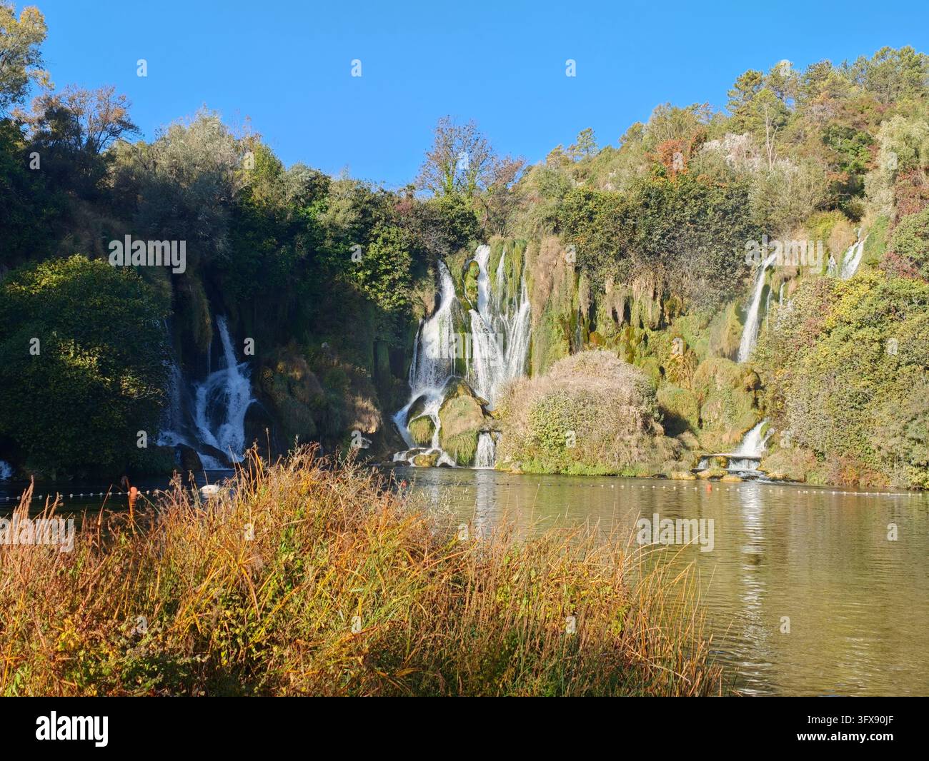 Herbstsonne über den Kravice-Wasserfällen, Bosnien und Herzegowina. Malerische Naturlandschaft mit kaskadierenden Tuffkaskaden und Herbstfarben. - Smartphone-aufgenommenes Stockfoto