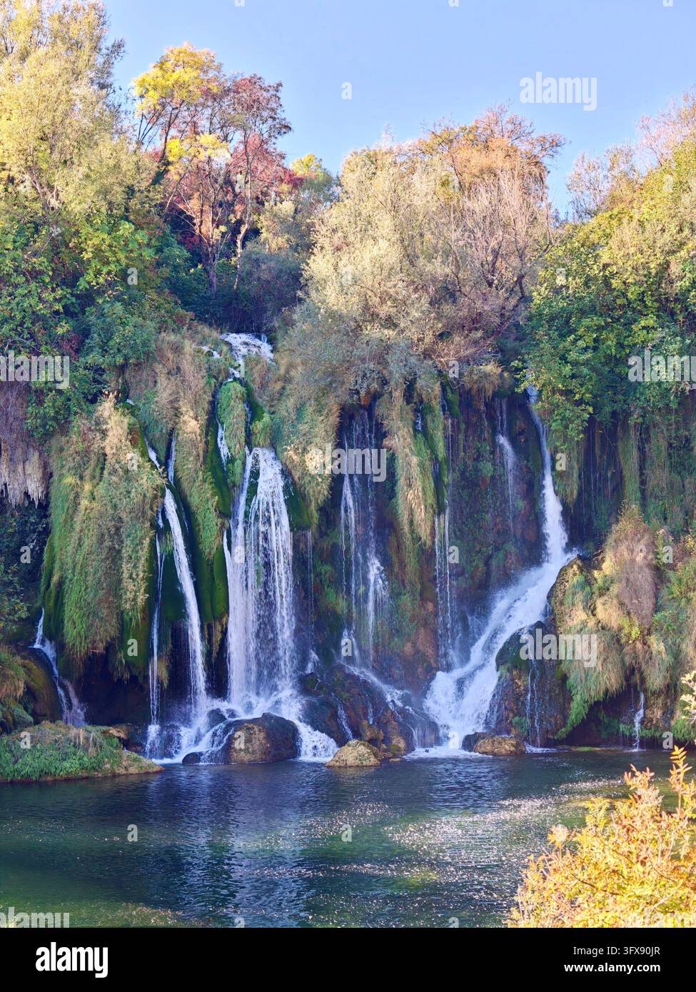 Herbstsonne über den Kravice-Wasserfällen, Bosnien und Herzegowina. Malerische Naturlandschaft mit kaskadierenden Tuffkaskaden und Herbstfarben. - Smartphone-aufgenommenes Stockfoto
