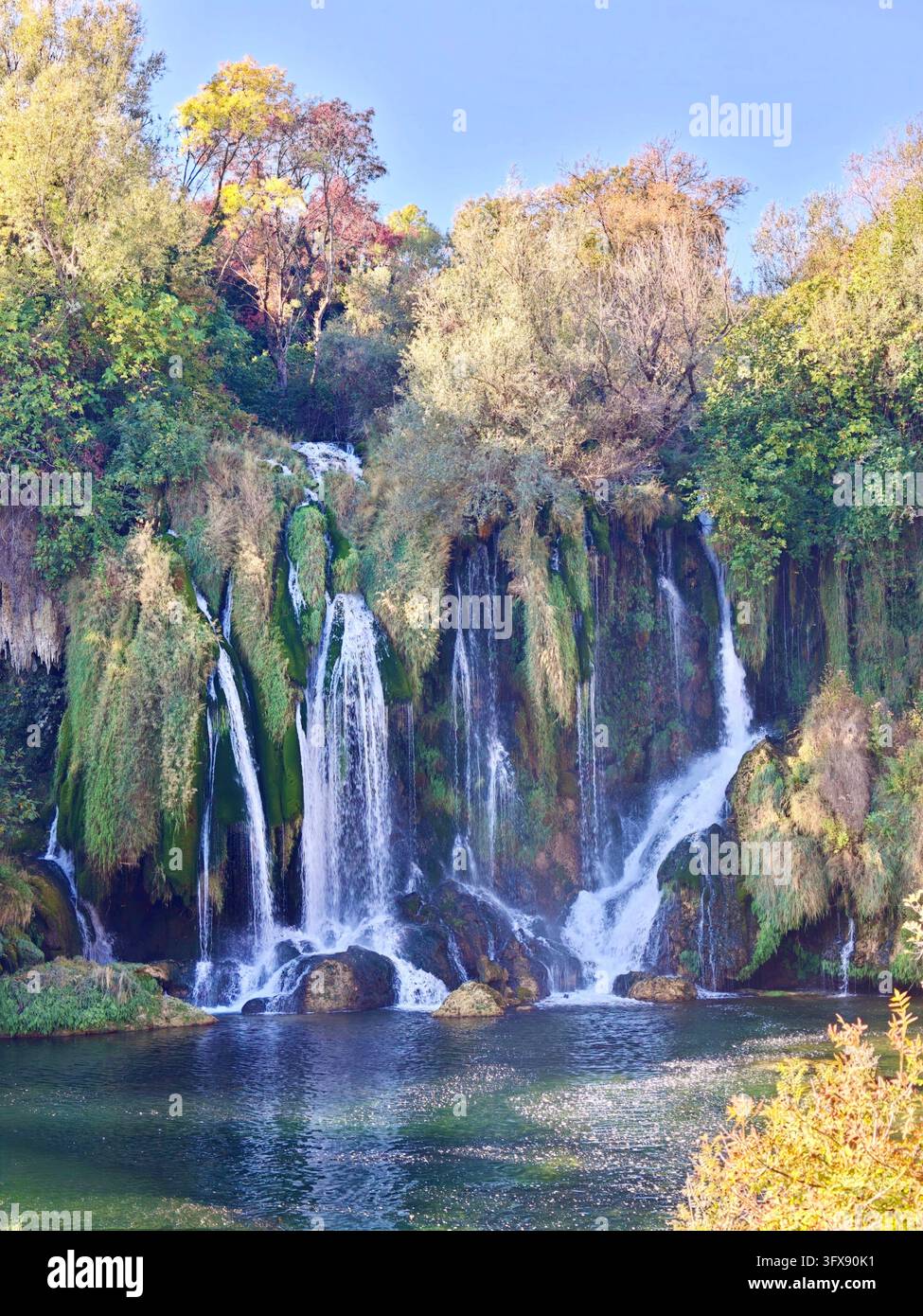 Herbstsonne über den Kravice-Wasserfällen, Bosnien und Herzegowina. Malerische Naturlandschaft mit kaskadierenden Tuffkaskaden und Herbstfarben. - Smartphone-aufgenommenes Stockfoto