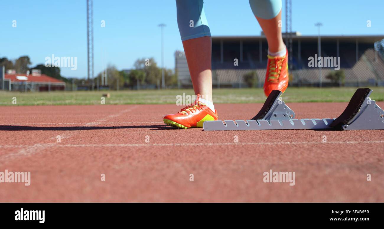 Junge Athletin, die sich auf der Laufbahn an einer Sportstätte für den Wettlauf bereitmacht. Sie ist bereit für das Rennen 4k Stockfoto